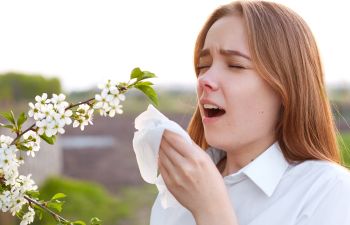 A young woman near the blooming trees sneezing cause of allergy.