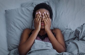 Sleepless mature Afro_american woman having difficulties with falling asleep lying in bed and covering her eyes with her hands